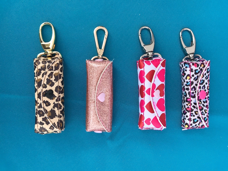 May include: Four small zippered pouches with key rings. The pouches are made of fabric and have different patterns: leopard print, pink glitter, hearts, and a multi-colored animal print.