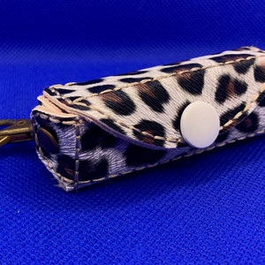 May include: A small, white and brown leopard print key chain with a white button and a gold metal hook.