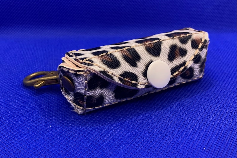 May include: A small, white and brown leopard print key chain with a white button and a gold metal hook.