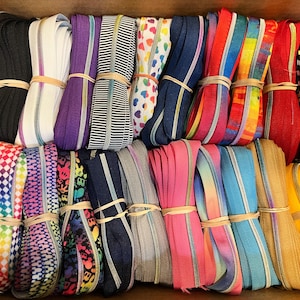 May include: A collection of 20 colorful zipper tapes with various patterns, including checkered, tie-dye, and hearts. The tapes are arranged in two rows, with each tape bundled together with a rubber band.