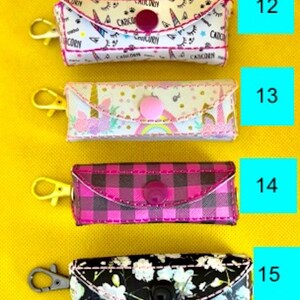 May include: Four different patterned zippered pouches with a button closure. The pouches are pink, black, white, and plaid. Each pouch has a gold or silver key ring attached.