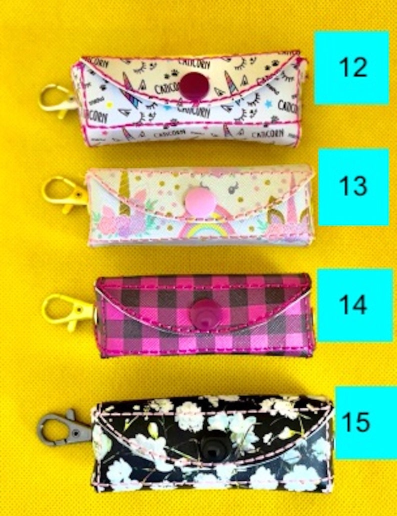 May include: Four different patterned zippered pouches with a button closure. The pouches are pink, black, white, and plaid. Each pouch has a gold or silver key ring attached.
