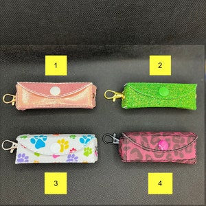 May include: Four different styles of small zippered pouches with key rings. The pouches are pink with gold glitter, green with green glitter, white with colorful paw prints, and pink with a leopard print.