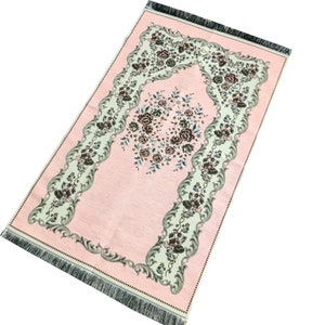 May include: A pink prayer rug with a floral design and a fringed border. The rug has a central arch with a floral motif.