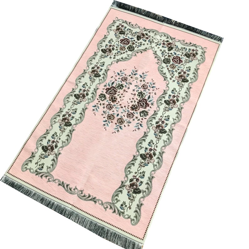 May include: A pink prayer rug with a floral design and a fringed border. The rug has a central arch with a floral motif.