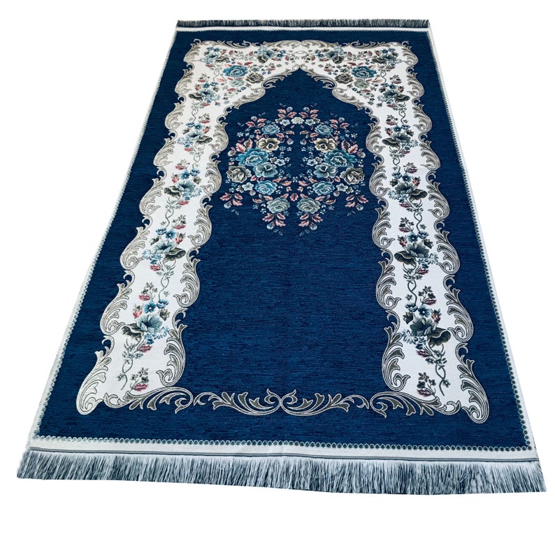 May include: A blue prayer rug with a white border and floral design. The rug has a fringed edge and a decorative arch in the center.