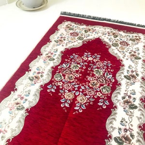 May include: Red prayer rug with a white floral design and a black fringe border.