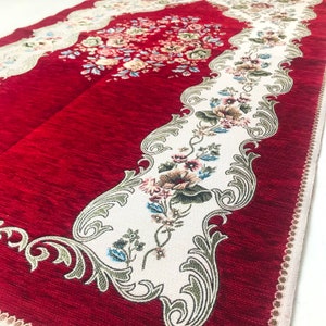 May include: Red prayer rug with a white floral design and intricate border. The rug has a soft, textured surface.