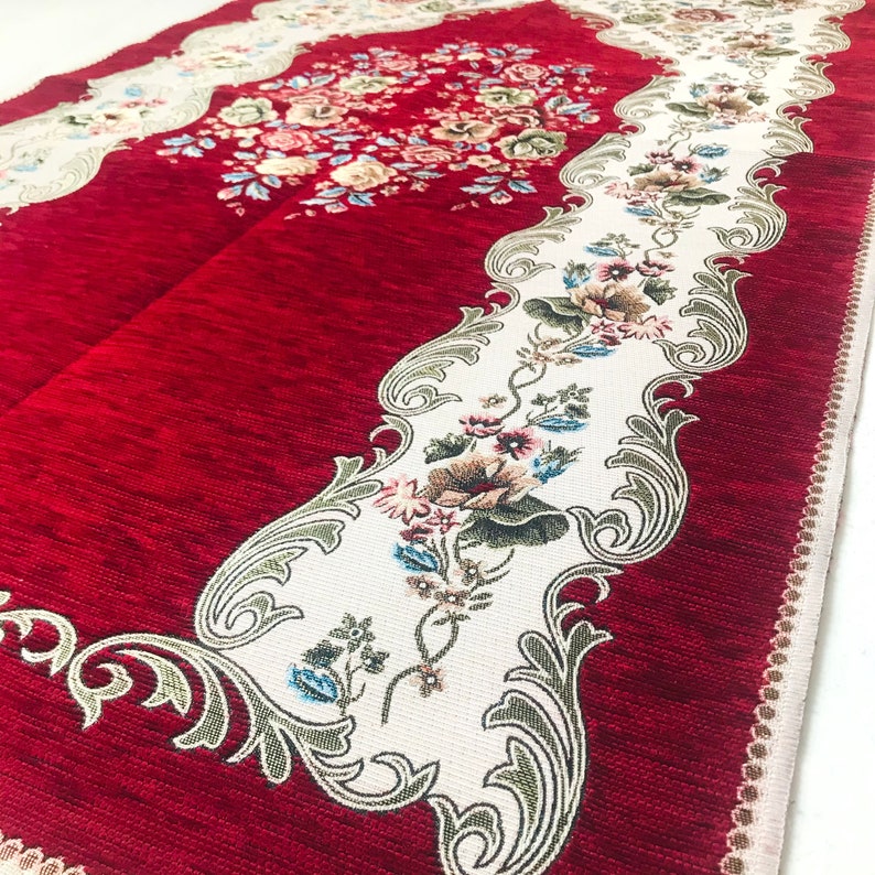 May include: Red prayer rug with a white floral design and intricate border. The rug has a soft, textured surface.