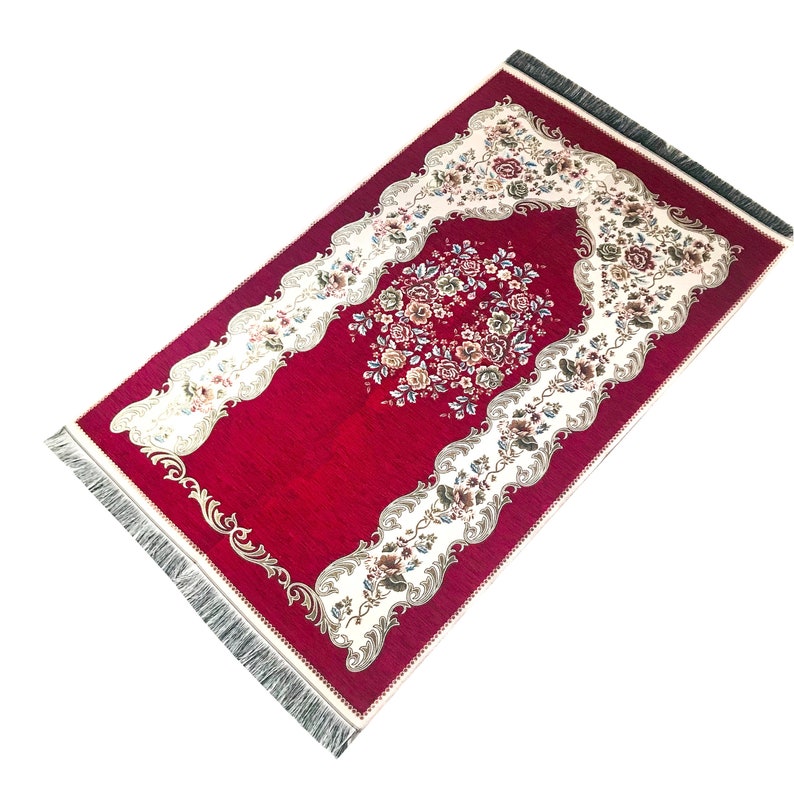 May include: A red prayer rug with a floral design and a white border. The rug has a fringe on all sides.