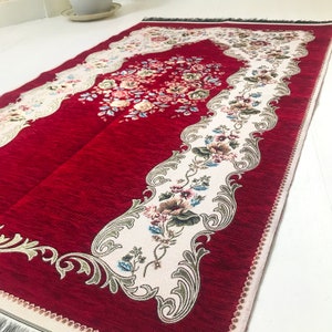 May include: Red prayer rug with a white floral design and a decorative border. The rug has a fringed edge.