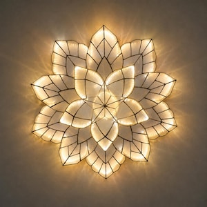 Op de afbeelding: Een wandlamp in de vorm van een meerlaagse bloem met een donker metalen frame en doorschijnende witte panelen. De structuur heeft een centraal sterpatroon omringd door stralende bloemblaadjes die een warme, zachte gloed van binnenuit uitstralen.