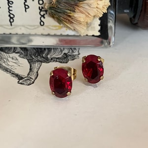 Könnte beinhalten: Ein Paar goldene Ohrstecker mit ovalen roten Edelsteinen.