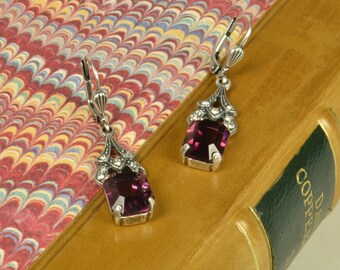 May include: A pair of silver dangle earrings with a purple gemstone and clear rhinestones.