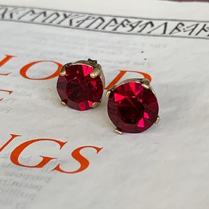 May include: A pair of red gemstone earrings with gold-toned settings. The earrings are on a white surface with text.
