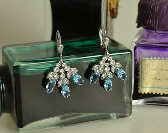 May include: A pair of silver-toned drop earrings featuring marquise-cut light blue stones and small round clear stones arranged in a fan-like pattern. The earrings have lever-back closures and a metallic finish with intricate detailing.