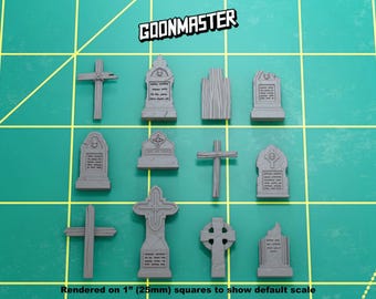 May include: A collection of eleven grey miniature tombstones and crosses arranged on a green cutting mat with 1-inch grid lines. The text GOONMASTER is visible at the top, and the text Rendered on 1" (25mm) squares is at the bottom.