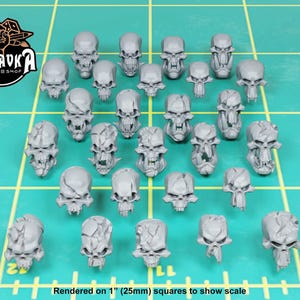May include: A collection of gray, skull-shaped miniatures arranged on a green grid. The skulls vary in design, some with cracked surfaces. The text "ZABAVKA WORKSHOP" is in the upper left corner. The text "Rendered on 1" (25mm) squares to show scale" is at the bottom.