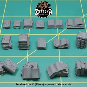 May include: A collection of miniature gray books in various sizes and styles, including closed, open, and stacked. The books are arranged on a green grid surface. The text "Rendered on 1" (25mm) squares to show scale" is visible.