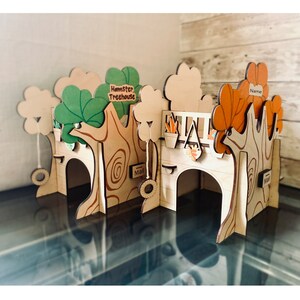 Puede incluir: Una casa de &aacute;rbol de h&aacute;mster de madera con un acabado de madera natural, con detalles de hojas verdes y naranjas. La casa del &aacute;rbol tiene m&uacute;ltiples niveles, dise&ntilde;os de &aacute;rboles recortados y un columpio. El texto en la casa del &aacute;rbol dice "Hamster Treehouse", "Mail" y "Name".