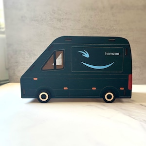 以下が含まれることがあります： 白い笑顔のAmazonロゴと側面に「hamzon」という文字が書かれた濃い緑色のオモチャの配送トラック。トラックは金色のリムが付いた黒い車輪です。