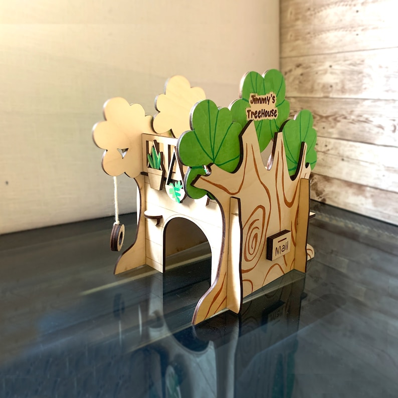 Puede incluir: Una casa en el &aacute;rbol de madera con un columpio, un peque&ntilde;o balc&oacute;n con plantas y el texto "Jimmy's Treehouse". La casa del &aacute;rbol tiene una ranura para el correo y est&aacute; pintada con detalles verdes y marrones.