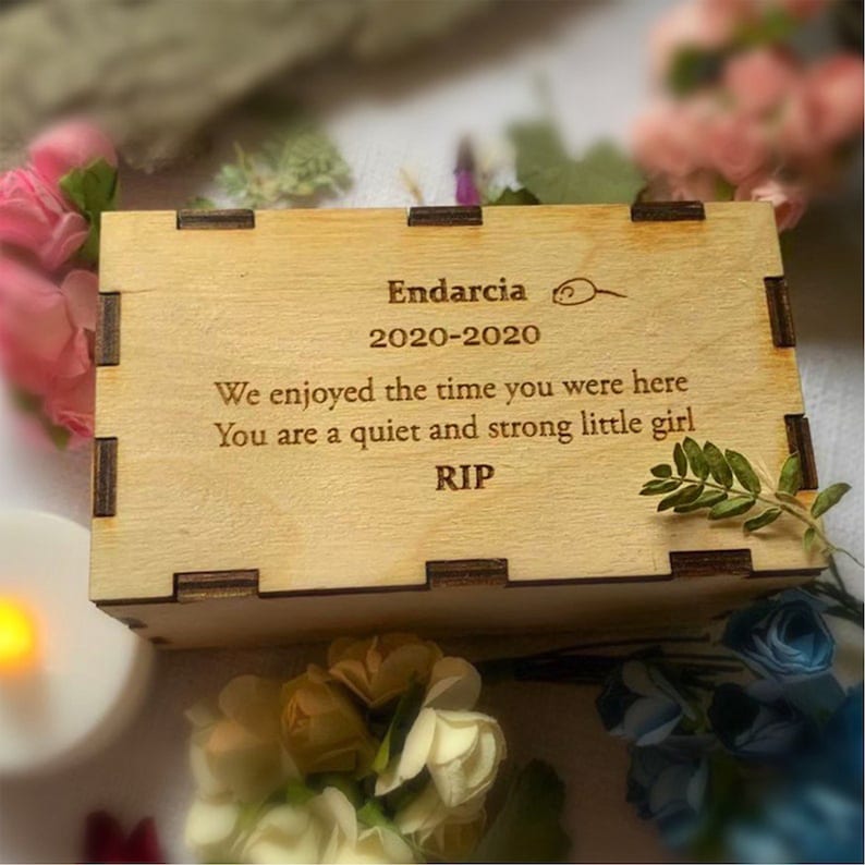 K&ouml;nnte beinhalten: Eine hellfarbene Holzkiste mit rechteckiger Form. Die Kiste hat ein lasergeschnittenes Design und enth&auml;lt den Text "Endarcia 2020-2020 We enjoyed the time you were here You are a quiet and strong little girl RIP."