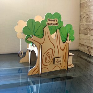 Puede incluir: Un buz&oacute;n de madera con forma de casa en el &aacute;rbol con un columpio y el texto "Jimmy's TreeHouse". La casa del &aacute;rbol tiene hojas verdes y un tronco marr&oacute;n con detalles de vetas de madera. Un peque&ntilde;o letrero dice "Mail".