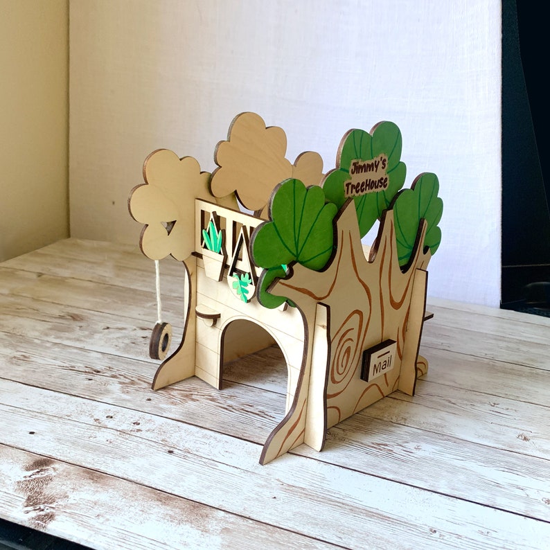 Puede incluir: Una casa en el &aacute;rbol de madera con columpio, arco y detalles en verde y marr&oacute;n. La casa en el &aacute;rbol tiene el texto "Jimmy's TreeHouse" en la parte superior y un peque&ntilde;o letrero de "Mail". La casa en el &aacute;rbol est&aacute; hecha de madera clara.