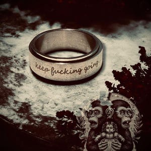 May include: A silver spinning ring with the words "keep fucking going" engraved on the band.