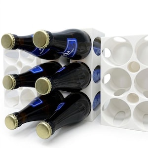 Puede incluir: Estantería modular blanca para vino que contiene varias botellas de vidrio oscuro con tapas doradas y etiquetas azules. La estantería está diseñada con aberturas circulares para sujetar las botellas de forma segura. También se ve una segunda estantería vacía.