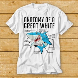 May include: White t-shirt with a cartoon shark design and the text "ANATOMY OF A GREAT WHITE." The shark is blue, with labels such as "Peekaboo Spheres" and "Ouchie No-No Zone" pointing to its features.