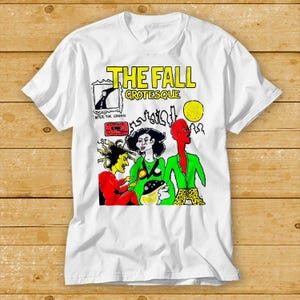 May include: White t-shirt featuring a colourful graphic print of a band called "The Fall" and the album title "Grotesque - After the Grapple".