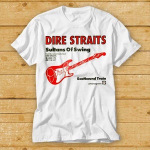 Può includere: T-shirt bianca con la scritta "DIRE STRAITS" in rosso sopra "Sultans Of Swing". Sotto, una grafica di chitarra rossa con il nome della band in corsivo. La maglietta include anche informazioni sull'album e sull'etichetta.