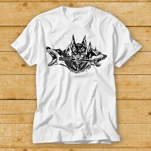Puede incluir: Camiseta blanca con un gráfico en blanco y negro de tres cabezas de perro con una espada en la boca.