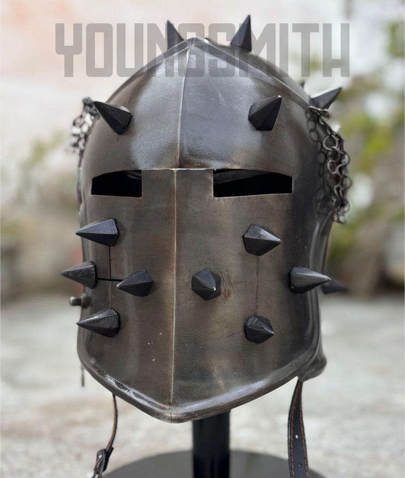 May include: A dark metal helmet with multiple black spikes and chainmail detail. The helmet has two eye slits and a leather strap. The word "YOUNGSMITH" is printed at the top of the image.