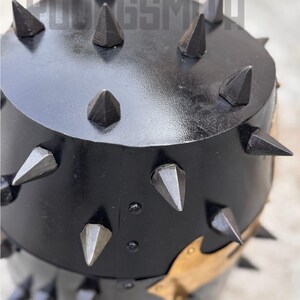 May include: Black metal object with numerous pointed spikes. The object has a rounded top and a cylindrical base. The spikes are evenly spaced around the top and sides. The text "YOUNGSMIT" is visible at the top.
