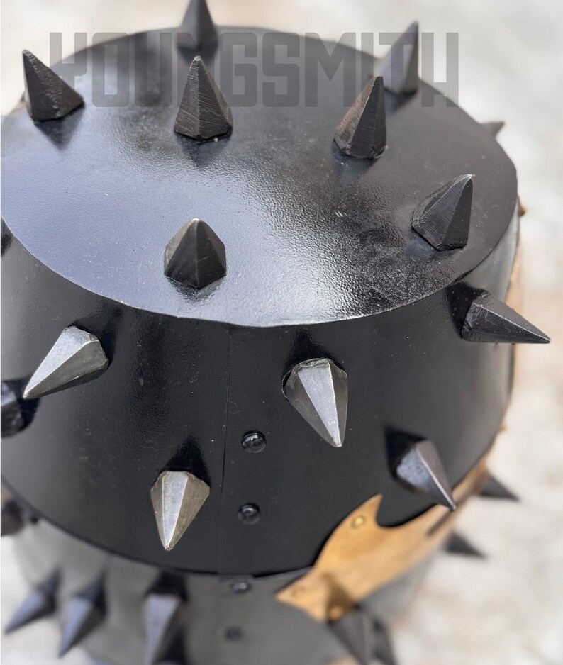 May include: Black metal object with numerous pointed spikes. The object has a rounded top and a cylindrical base. The spikes are evenly spaced around the top and sides. The text "YOUNGSMIT" is visible at the top.