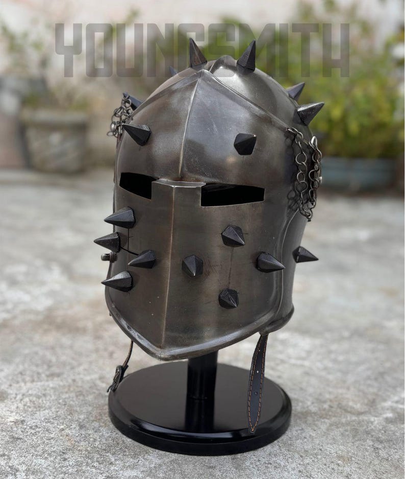 May include: A metallic, spiked helmet with a dark finish, displayed on a black stand. The helmet features multiple black spikes and a chain detail. The text "YOUNG SMITH" is visible at the top.