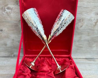 Könnte beinhalten: Zwei silberne Champagnerflöten mit aufwendigen floralen Designs, präsentiert in einer roten Samtbox.