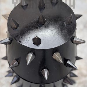May include: A black, spiked metal object with a rounded top and a cylindrical base. The spikes are various sizes and shapes, some with a metallic sheen. The text "YUNSMITH" is visible at the top.
