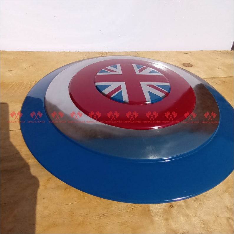 May include: A blue, red, and white shield with a Union Jack design in the center. The shield is made of metal and has a shiny finish.