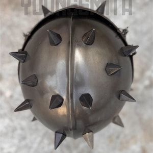 May include: A dark gray metal helmet with numerous pointed spikes. The helmet has a rounded shape with a central ridge and the text "YOUNGSMITH" across the top.