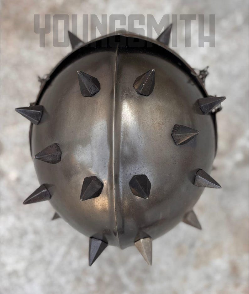May include: A dark gray metal helmet with numerous pointed spikes. The helmet has a rounded shape with a central ridge and the text "YOUNGSMITH" across the top.