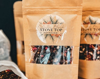 May include: A brown paper bag with a clear window showing a blend of dried spices and berries. The bag has a label that reads "Winter Blend Stove Top Potpourri".
