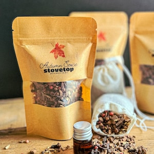 May include: A brown paper bag with a clear window showing a blend of spices inside. The bag has a label that says "Autumn Spice Stovetop Potpourri". There is a small bottle of essential oil and a white muslin bag filled with spices next to the bag.