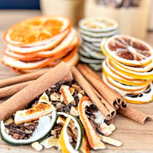 May include: A close-up of a mixture of dried orange and lime slices, cinnamon sticks, and other spices. The ingredients are arranged on a wooden surface.