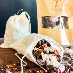 May include: A white muslin bag filled with coffee beans, candy canes, and spices. The bag is spilling its contents onto a wooden surface. The bag is labeled "SERVE YOUR COFFEE".