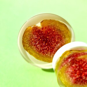 May include: Two clear resin ornaments with a dried fig slice inside. The fig slices are translucent and show the red flesh of the fruit.