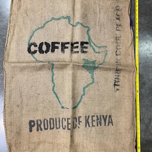 May include: A burlap coffee sack with the word "COFFEE" in black letters over a green outline of Africa. The words "PRODUCE OF KENYA" are printed below. The sack is approximately 40 inches long.